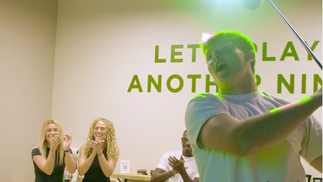 Group of people playing in one of Another Nine's sim suites in front of a sign that says 'Let's Play Another Nine'.